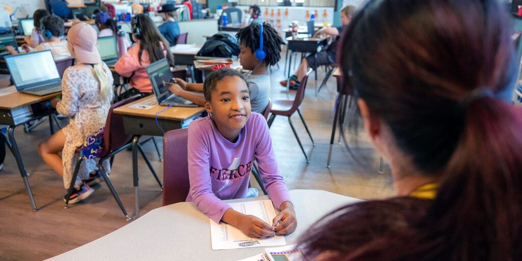 Smiling student working with a teacher at a desk in an elementary classroom