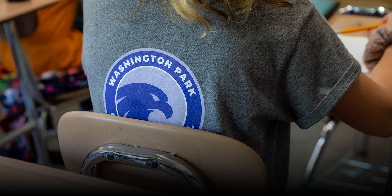 Picture of the Washington Park Community School logo on the back of a shirt of a student sitting at a desk